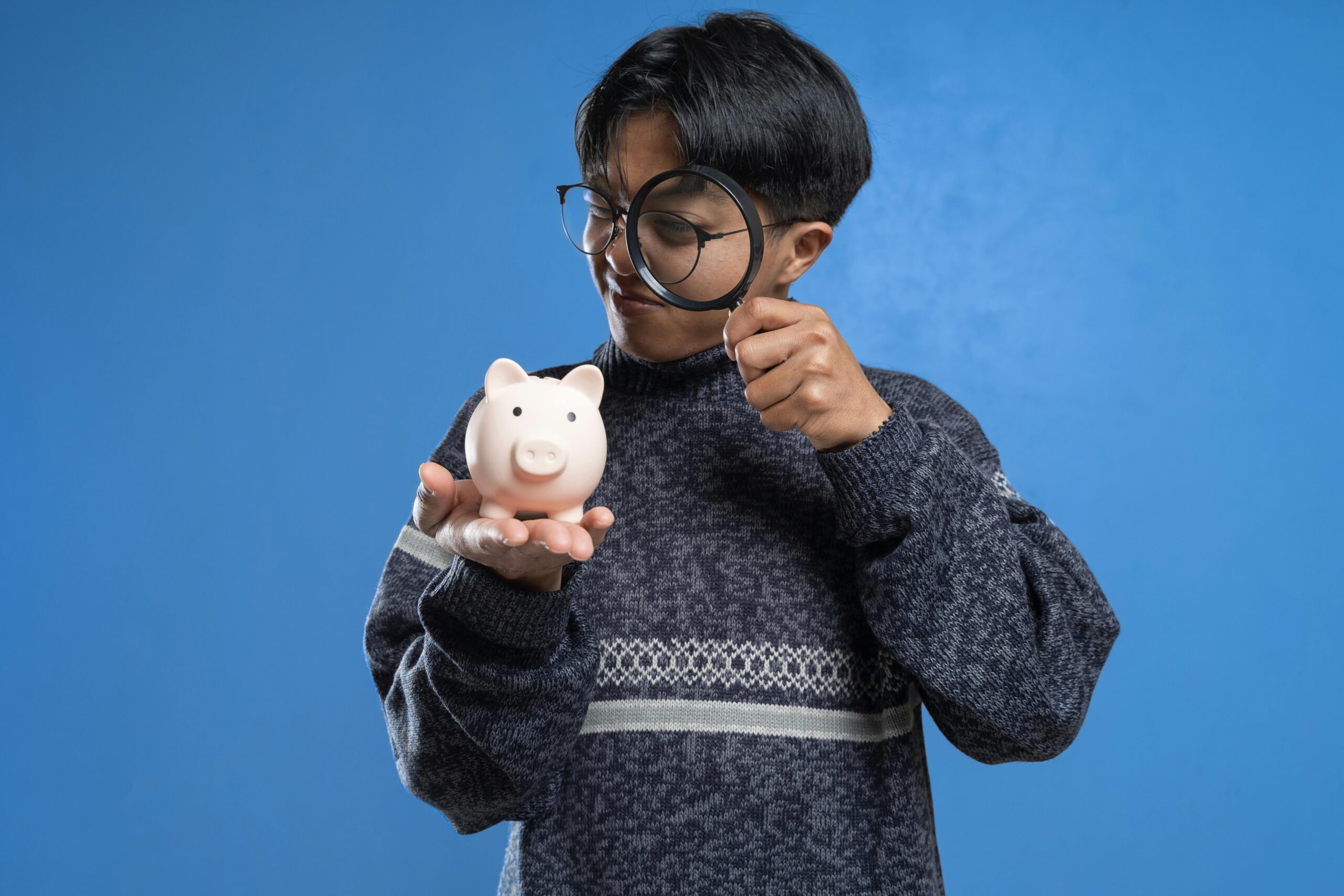 boy looking at piggy bank through magnifying glass